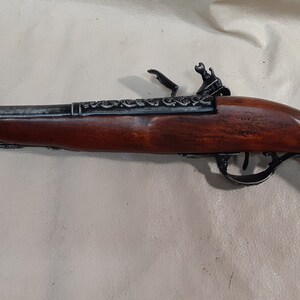 May include: A black flintlock pistol with a wooden handle. The pistol has intricate metalwork on the barrel and a decorative design on the hammer.
