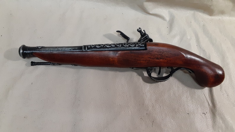 May include: A black flintlock pistol with a wooden handle. The pistol has intricate metalwork on the barrel and a decorative design on the hammer.