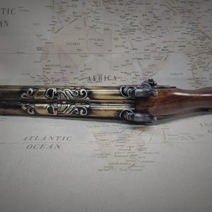 May include: A gold and brown triple-barreled pistol with skull and scrollwork details. The pistol is made of metal and wood and has a black finish.