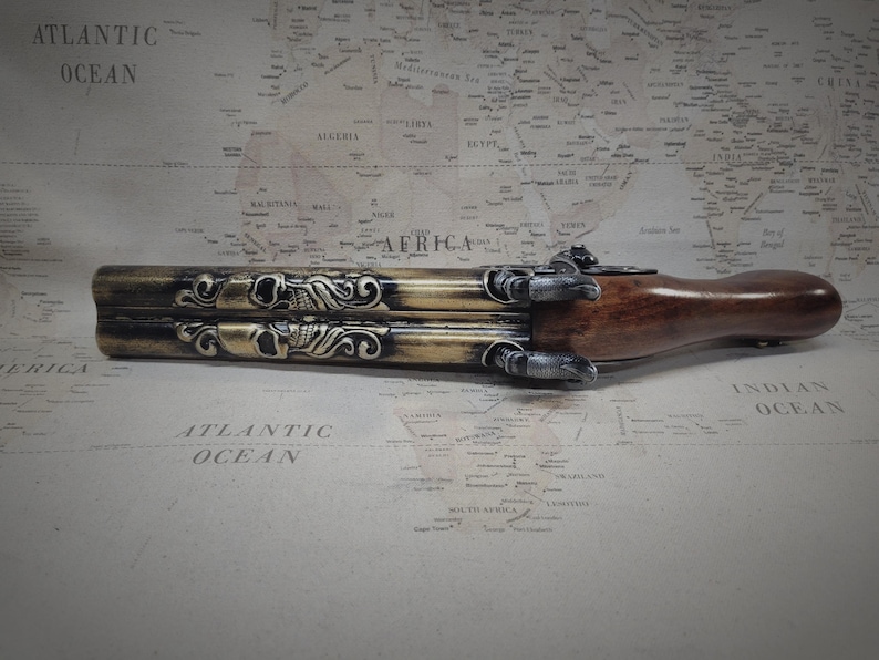 May include: A gold and brown triple-barreled pistol with skull and scrollwork details. The pistol is made of metal and wood and has a black finish.