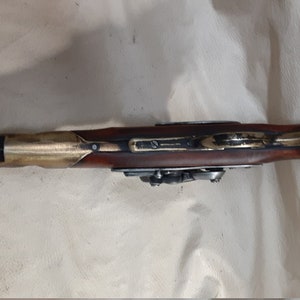 Op de afbeelding: Een antiek vuursteenpistool met een houten handvat en messing accenten.