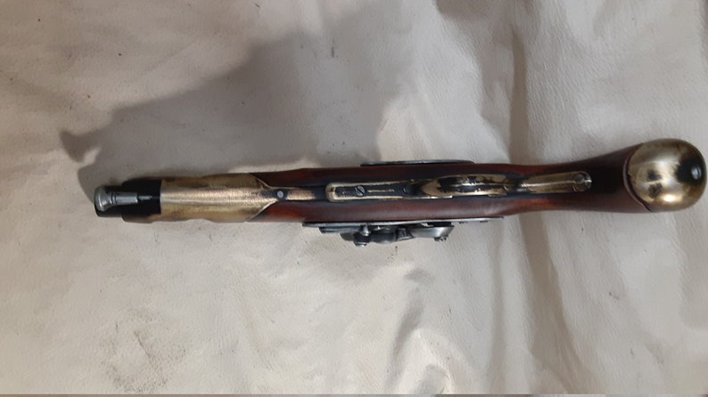 Op de afbeelding: Een antiek vuursteenpistool met een houten handvat en messing accenten.
