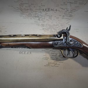May include: A decorative, antique-style flintlock pistol with a brass barrel and a wooden stock. The pistol has intricate engravings on the metal and a detailed design on the stock.