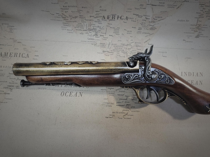 May include: A decorative, antique-style flintlock pistol with a brass barrel and a wooden stock. The pistol has intricate engravings on the metal and a detailed design on the stock.