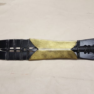 May include: A black and gold spear with a leather wrap and a pointed tip. The spear is about 24 inches long.