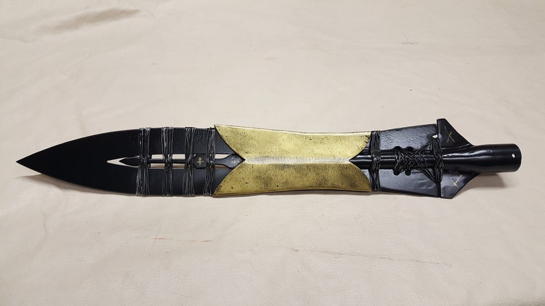 May include: A black and gold spear with a leather wrap and a pointed tip. The spear is about 24 inches long.