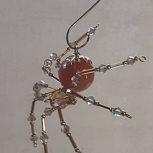 May include: A gold spider ornament with a peach-colored glass bead body and clear crystal accents.