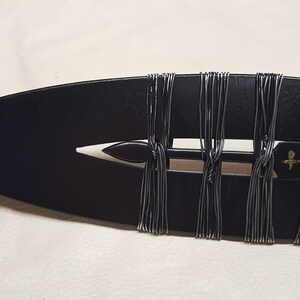 May include: Close-up of a black spearhead with a gold tip. The spearhead is wrapped with black wire.
