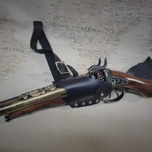 May include: A black leather holster with a decorative brass and wood pistol. The holster has a strap that can be worn over the shoulder.