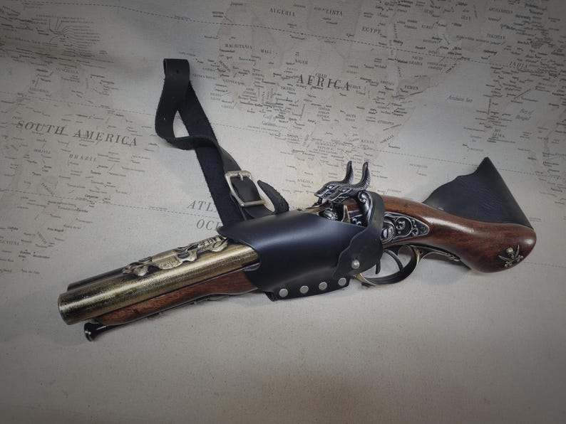 May include: A black leather holster with a decorative brass and wood pistol. The holster has a strap that can be worn over the shoulder.