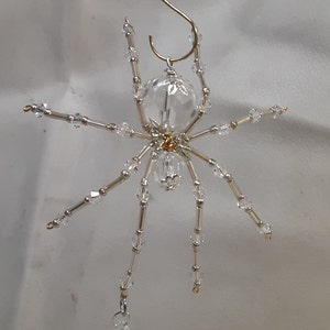May include: A crystal spider ornament with a gold hanger. The spider has a clear crystal body and legs with silver beads.