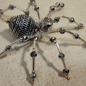 May include: A silver and black beaded spider ornament with a detailed, patterned body. The spider has eight legs with silver wire and black beads.