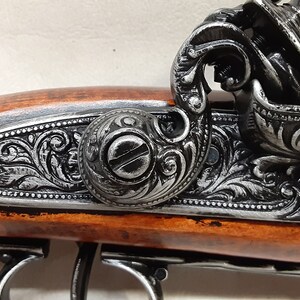 May include: A close-up of a black and silver antique-style pistol with intricate engravings on the barrel and a wooden handle.