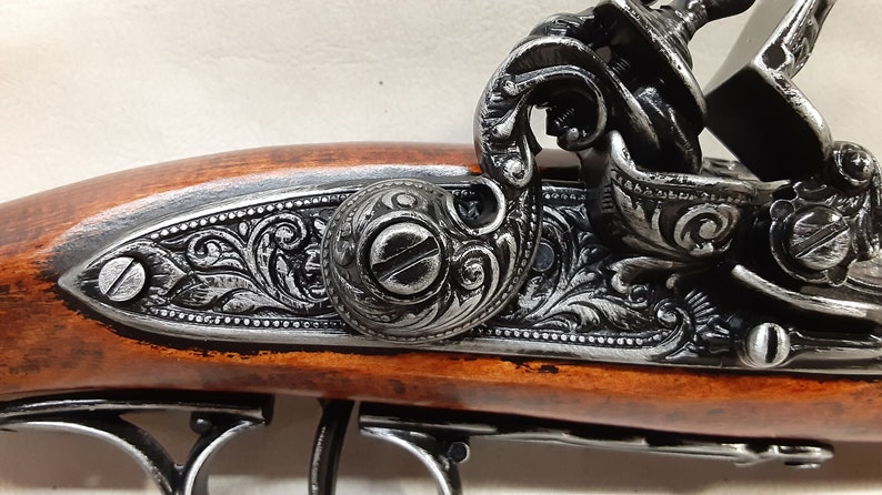 May include: A close-up of a black and silver antique-style pistol with intricate engravings on the barrel and a wooden handle.