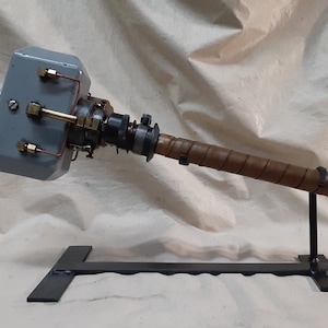 May include: A grey metal hammer with a brown leather wrapped handle, mounted on a black metal stand.