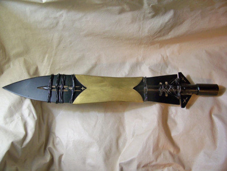 May include: A black and gold spear with a leather wrap and a pointed tip. The spear is made of metal and has a decorative design.