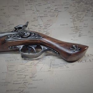 May include: A detailed, ornate, silver-plated pistol with a wooden stock and a skull and crossbones design on the grip. The pistol is resting on a vintage world map.
