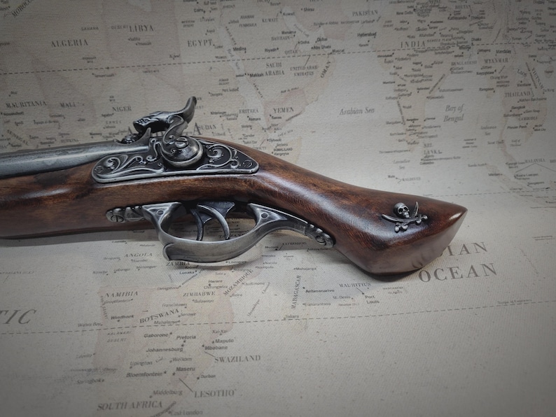 May include: A detailed, ornate, silver-plated pistol with a wooden stock and a skull and crossbones design on the grip. The pistol is resting on a vintage world map.