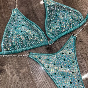 May include: Teal and silver sequined bikini with rhinestones. The bikini top has a triangle shape and the bottom is a high-cut style.