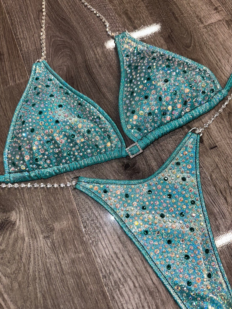 May include: Teal and silver sequined bikini with rhinestones. The bikini top has a triangle shape and the bottom is a high-cut style.
