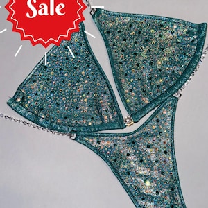 May include: Teal bikini with rhinestones and a silver chain. The bikini top is a triangle style and the bottom is a thong style.