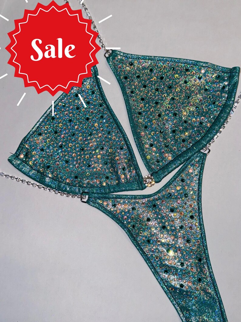 May include: Teal bikini with rhinestones and a silver chain. The bikini top is a triangle style and the bottom is a thong style.