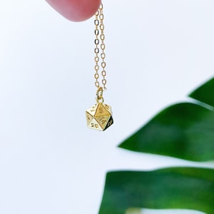 Puede incluir: Un collar de cadena dorada con un colgante de dado de 20 caras de oro.