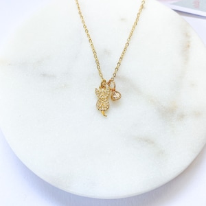 May include: A gold chain necklace with a small, clear crystal cat charm and a small, clear crystal heart charm.