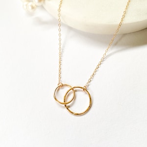 Puede incluir: Un collar de cadena dorada con un delicado colgante que presenta dos círculos entrelazados. Los círculos están martillados para un aspecto texturizado.