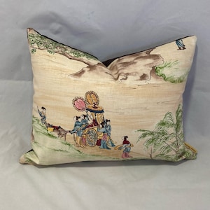 Puede incluir: Una almohada decorativa con fondo beige y borde marrón. La almohada presenta una ilustración colorida de personas con ropa tradicional montando en un carruaje tirado por bueyes. La escena se desarrolla en un contexto de montañas y árboles.