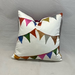 May include: White pillow with a colorful bunting pattern. The bunting is made of triangles in shades of red, orange, yellow, green, blue, and purple.