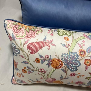 May include: Two decorative cushions. The front cushion features a white background with a floral pattern in pink, orange, green, and blue. The second cushion is a solid navy blue.