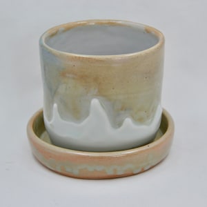 May include: A ceramic planter with a white glaze and a light brown glaze. The planter has a matching saucer.