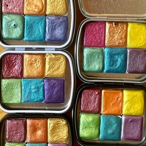 Watercolor tins. Each tin includes six half pans with different colors of shimmering and glittering paint.