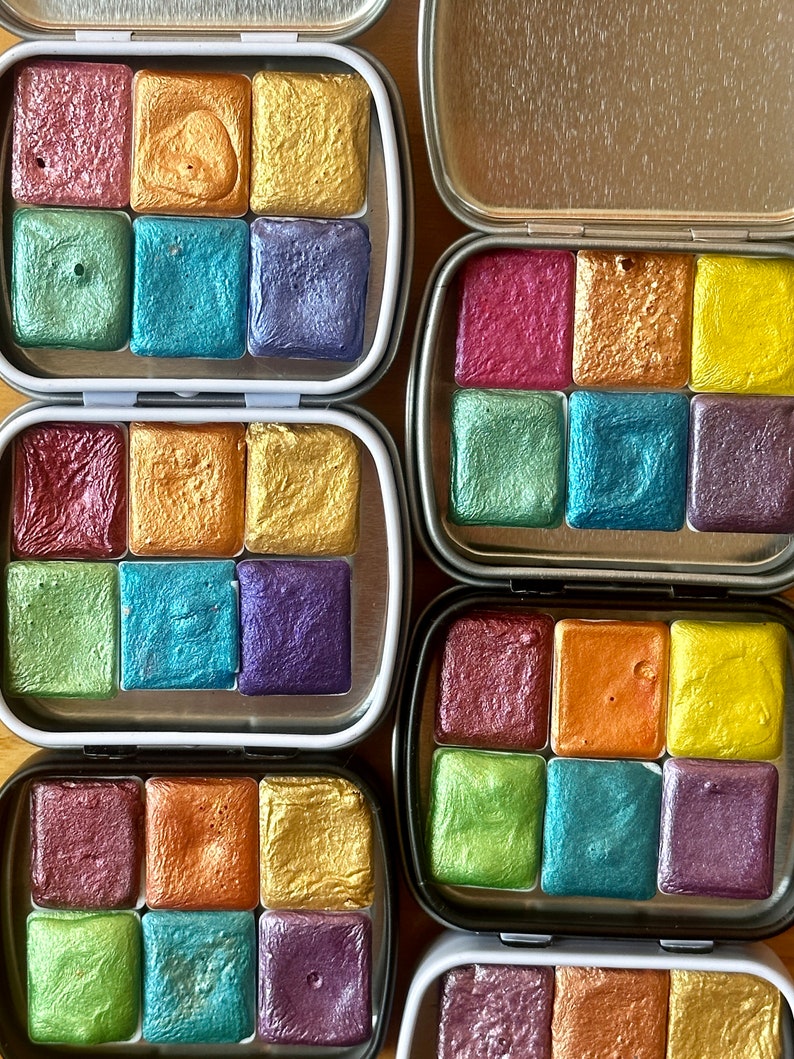 Watercolor tins. Each tin includes six half pans with different colors of shimmering and glittering paint.