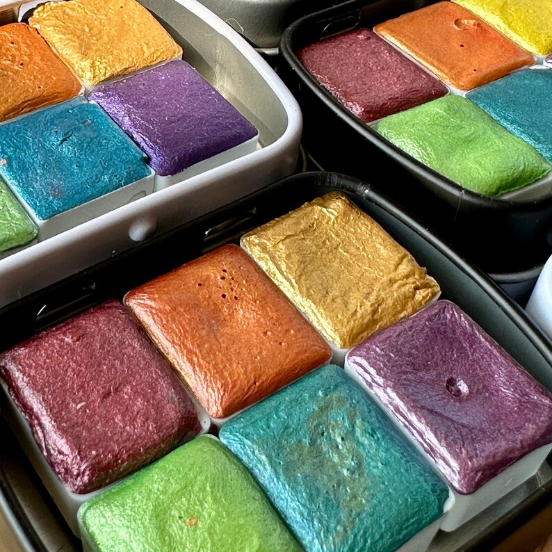 Watercolor tins. Each tin includes six half pans with different colors of shimmering and glittering paint.