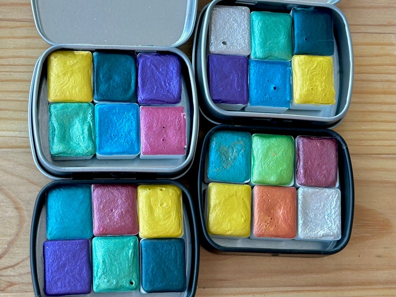 Four watercolor tins. Each tin includes six half pans with different colors of shimmering and glittering paint.
