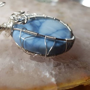 May include: A silver wire wrapped pendant featuring a blue and white opal stone.