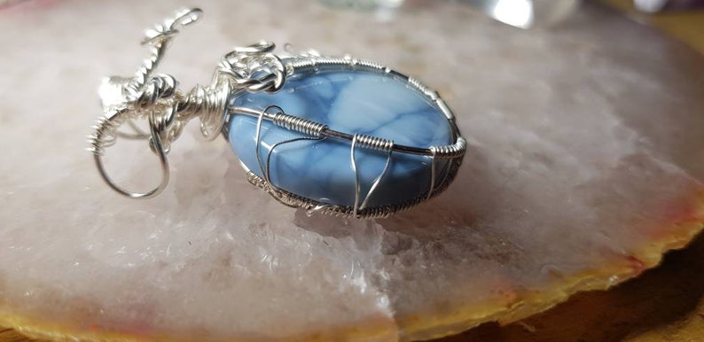 May include: A silver wire wrapped pendant featuring a blue and white opal stone.