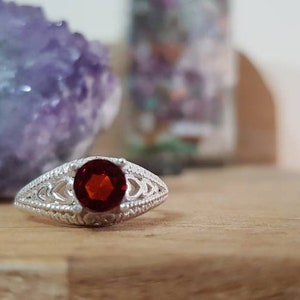 Puede incluir: Un anillo de plata con una piedra preciosa roja engastada en un diseño de filigrana.