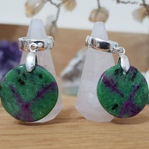 Pode incluir: Um par de brincos de argola de prata com pingentes de pedras preciosas verdes e roxas. As pedras preciosas são redondas e têm um padrão manchado.