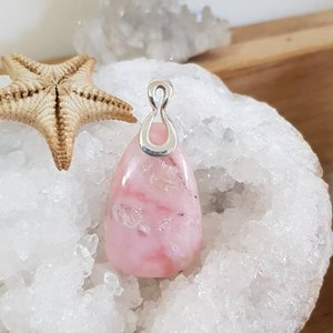 May include: A pink opal pendant with a silver bail. The pendant is sitting on a bed of white crystals.