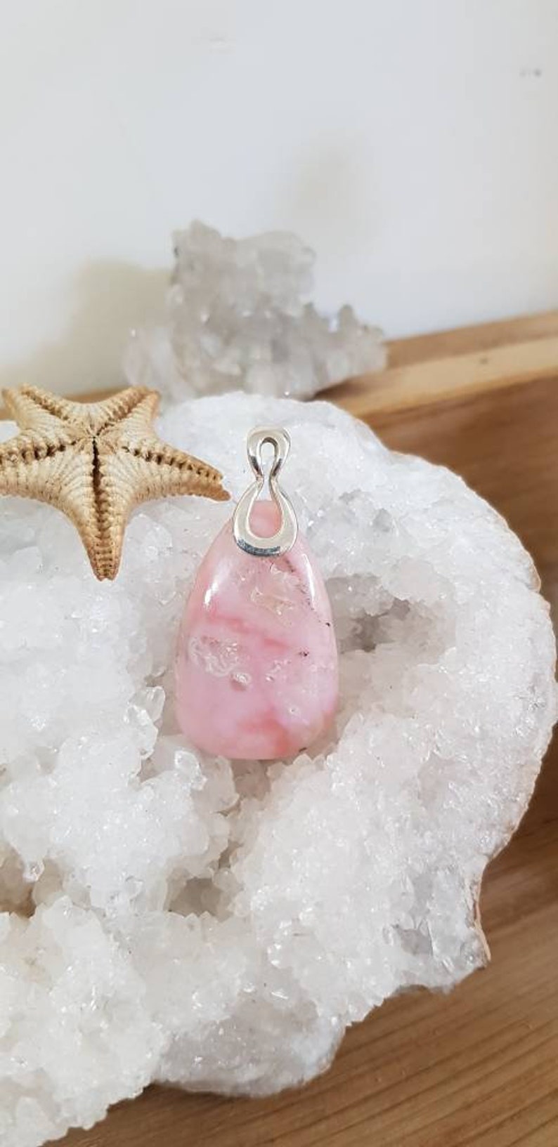 May include: A pink opal pendant with a silver bail. The pendant is sitting on a bed of white crystals.