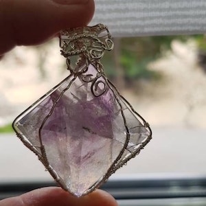 May include: A purple and clear crystal pendant with silver wire wrapping. The crystal is shaped like a square with rounded edges.