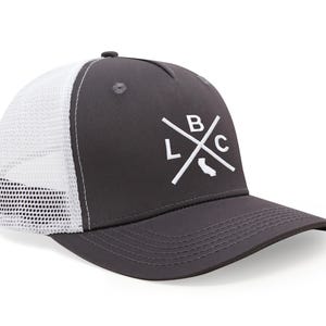 May include: A charcoal gray trucker hat with a white mesh back and a curved brim. The front features a white graphic of crossed lines with the letters "LBC" and a California outline.