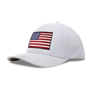 Könnte beinhalten: Eine weiße Baseballkappe mit einem aufgestickten amerikanischen Flaggenaufnäher. Die Flagge zeigt rote und weiße Streifen und einen blauen Bereich mit weißen Sternen. Die Kappe hat einen gebogenen Schirm und eine perforierte Seitenwand.