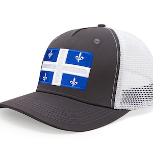 May include: A charcoal gray trucker hat with a white mesh back and a curved brim. The front panel features a patch with the flag of Quebec, a blue and white design with four fleur-de-lis.