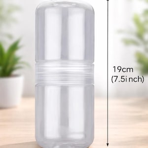 Puede incluir: Un recipiente cilíndrico transparente, de 7,5 cm de ancho y 19 cm de alto, con tapa y base atornillables. El recipiente está hecho de plástico transparente y está diseñado para contener objetos. El recipiente está sobre una superficie de madera.