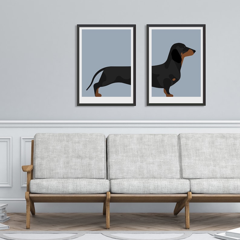 May include: Two framed wall art prints featuring a split illustration of a black and tan dachshund. The left print shows the rear of the dog, while the right print shows the front, both set against a solid light blue background in black frames.