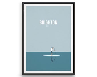 Könnte beinhalten: Ein minimalistisches Poster in Blau- und Weißtönen. Das Poster zeigt eine Person beim Paddelsurfen auf einem Gewässer. Der Text "BRIGHTON 2023" befindet sich oben auf dem Poster.